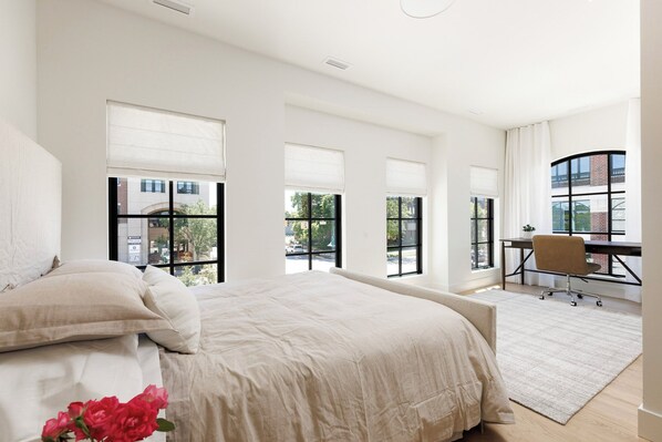 A bedroom with a large bed, a desk, and a chair. There are multiple windows with blinds. - Waterfront Luxury Home Downtown Traverse City (Traverse City)