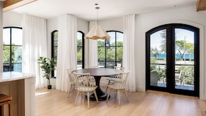 A dining area with a round table, six chairs, a hanging light fixture, and large windows with curtains. - Waterfront Luxury Home Downtown Traverse City (Traverse City)