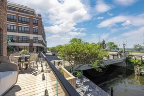 A wooden deck with outdoor furniture, a bridge over a water channel, and a building with multiple floors and windows. - Waterfront Luxury Home Downtown Traverse City (Traverse City)