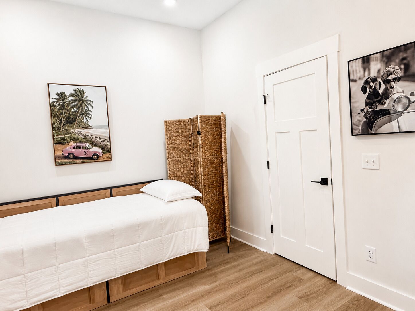 Un dormitorio con una cama individual, un separador tejido, una puerta y un cuadro en la pared.