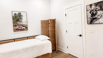 Un dormitorio con una cama individual, un separador tejido, una puerta y un cuadro en la pared.