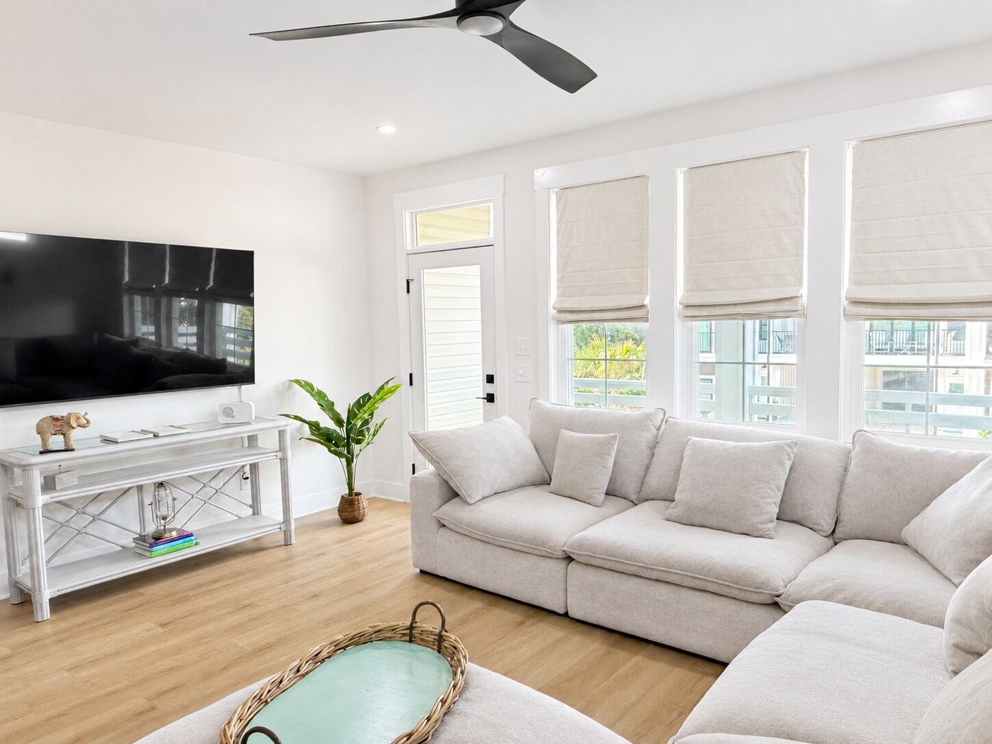 A modern living room with a flat-screen TV, a white sofa, a coffee table, and a ceiling fan.