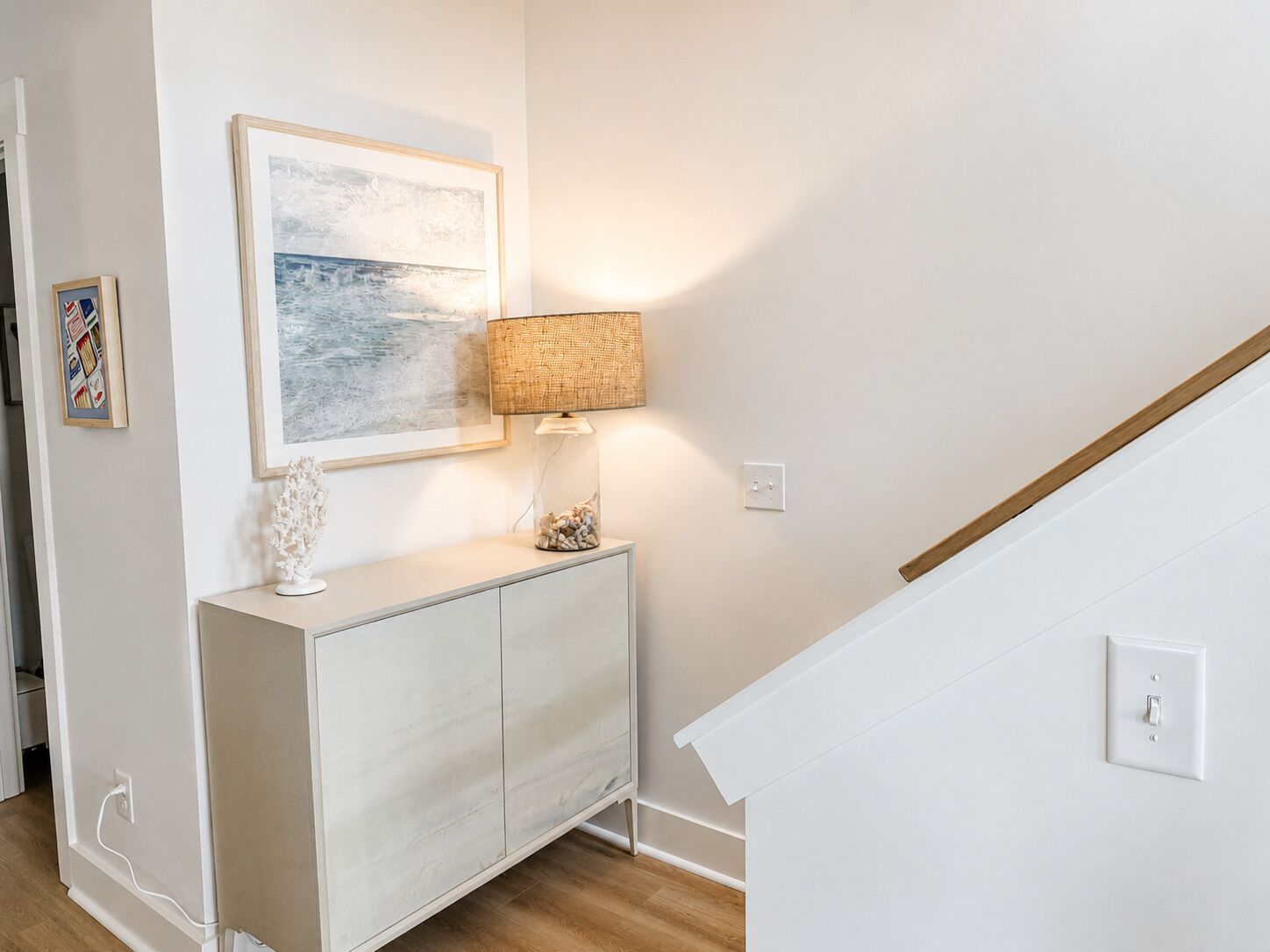 Una habitación con un armario blanco, un cuadro enmarcado, una lámpara y una escalera.