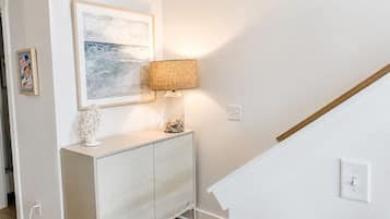 Una habitación con un armario blanco, un cuadro enmarcado, una lámpara y una escalera.