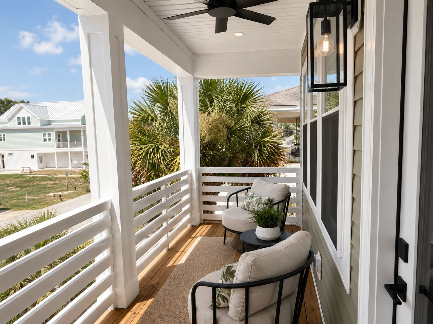 A covered porch with a ceiling fan, white railings, and two chairs with cushions.