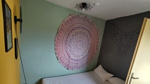 Un dormitorio con cama, un tapiz en la pared, un ventilador de techo y una puerta.