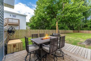 A deck with a fire pit table and chairs, surrounded by a wooden fence and a grassy yard. - TMD Estate. Two Homes. One Private Retreat. Minutes from Downtown and The Beach (Wilmington)