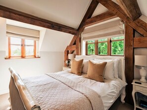 Ein Schlafzimmer mit einem Bett, Holzbalken, einem Fenster und einem Nachttisch.