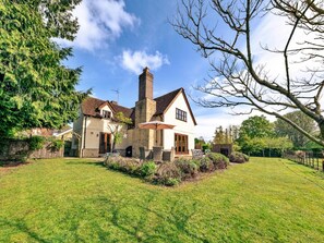 A two-story house with a chimney, a patio with outdoor furniture, and a well-maintained lawn. - Luxury Cotswolds Cottage for 7 (Tewkesbury)