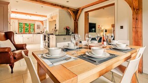 A dining area with a wooden table set for a meal, a leather chair, and a kitchen in the background. - Luxury Cotswolds Cottage for 7 (Tewkesbury)
