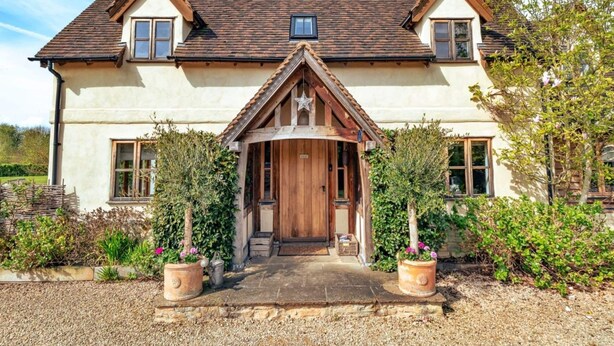 A two-story house with a gabled roof, a central entrance with a wooden door, and a small window above the door. - Luxury Cotswolds Cottage for 7 (Tewkesbury)