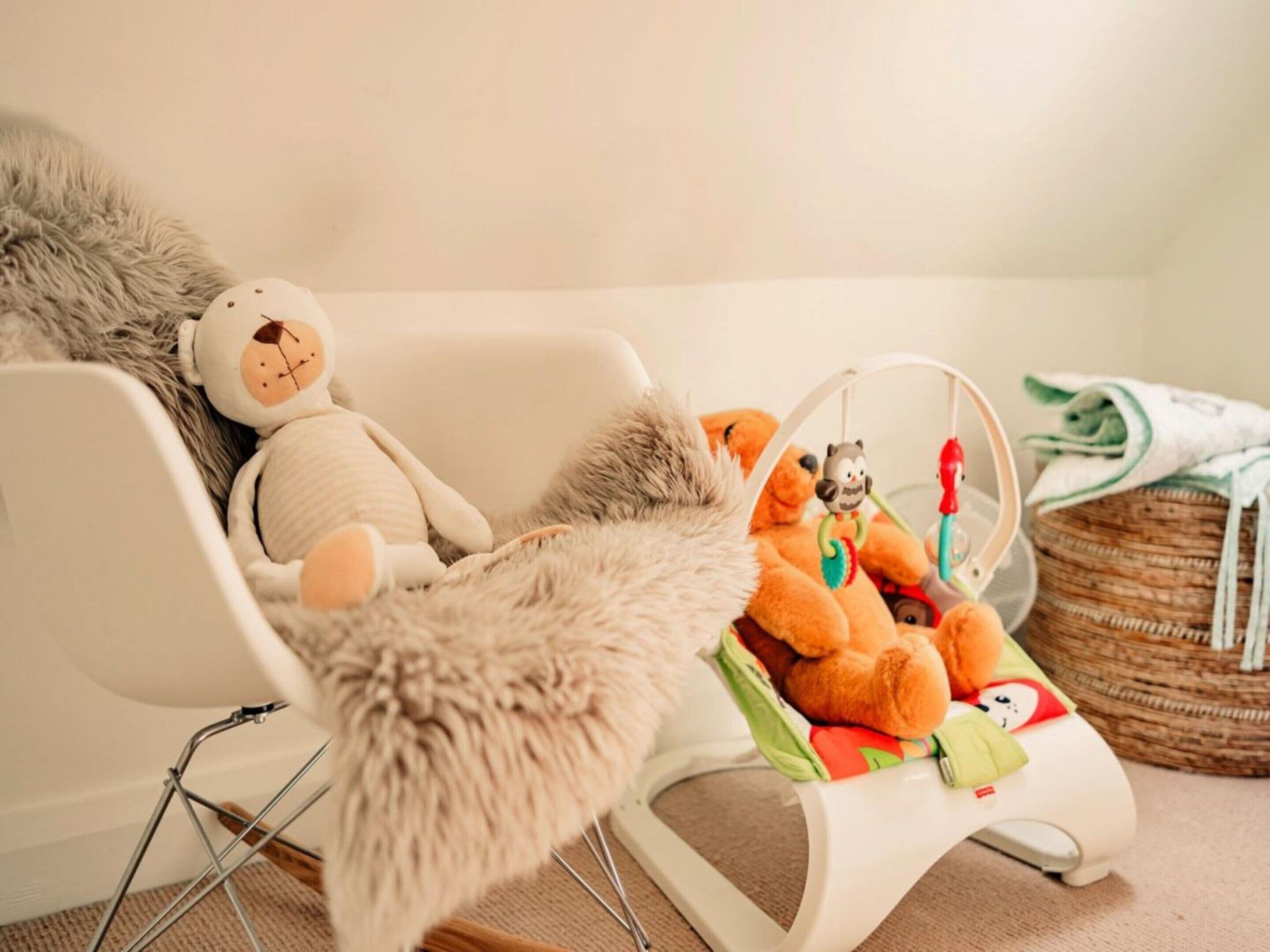 A room with a white chair, a fluffy rug, and a baby play area with toys and a hanging mobile.