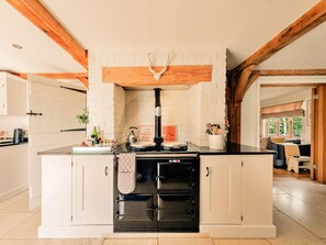 A kitchen with a central island, white cabinetry, a black stove, and exposed wooden beams. - Luxury Cotswolds Cottage for 7 (Tewkesbury)