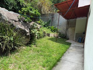 Una piccola area esterna recintata, con un muro in cemento, un'area verde e una struttura con tetto rosso.