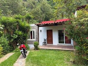 Una pequeña casa con techo rojo, un patio empedrado y una motocicleta estacionada adelante.