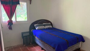 A single bed with a blue bedspread, a dark headboard, and a window with red curtains. - Casa Verde Panajachel (Panajachel)