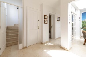 A hallway with a staircase, white doors, and a view of a garden through a window. - Villa Aureo with private pool (La Caleta)