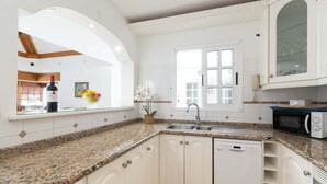 Een keuken met witte kastjes, granieten aanrecht, vaatwasser, magnetron en een raam met uitzicht.