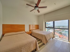 Ein Hotelzimmer mit zwei Betten, einem Deckenventilator, einem Nachttisch und einem großen Fenster mit Blick auf die Stadt.