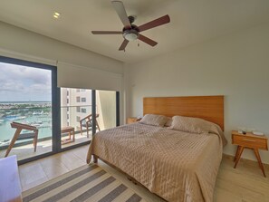 A bedroom with a bed, a nightstand, a wooden headboard, a ceiling fan, and a view of a marina through a sliding glass door. - Luxury Oceanfront Condo | Marina Resort | 3BR | Pools | Sleeps 10 (Progreso)