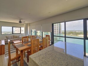 Ein modernes Wohnzimmer mit Essbereich, großen Fenstern und einem Balkon mit Blick auf eine Stadtlandschaft.