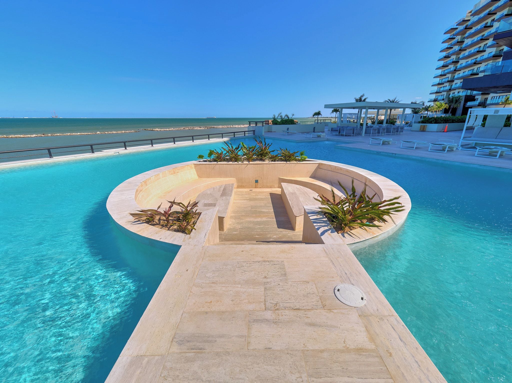A pool with a curved design, surrounded by lounge chairs and a building with balconies.