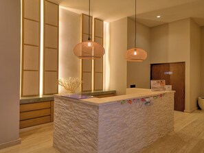 A reception desk with a stone-textured counter, two woven pendant lights, and a wooden door with a sign.