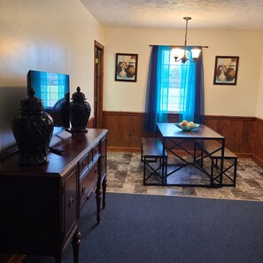 A dining area with a wooden table and bench, a dark wooden dresser, and two wall-mounted paintings.
