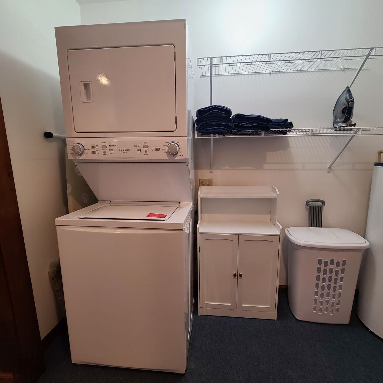 Un espace réduit dédié à la buanderie, comprenant un lave-linge, un étendoir et un petit meuble de rangement.