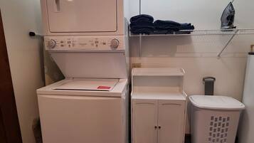 Un espace réduit dédié à la buanderie, comprenant un lave-linge, un étendoir et un petit meuble de rangement.