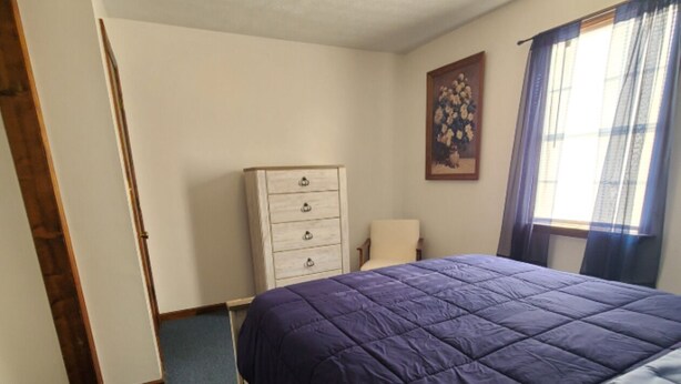 Une chambre à coucher avec un lit, une commode, une chaise et une fenêtre avec des rideaux.