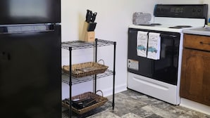 Une cuisine avec un réfrigérateur noir, une cuisinière blanche et une étagère en métal avec des paniers.