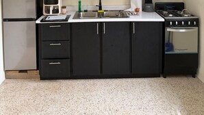 Uma cozinha compacta com armários pretos, geladeira de aço inoxidável, cafeteira e fogão a gás.
