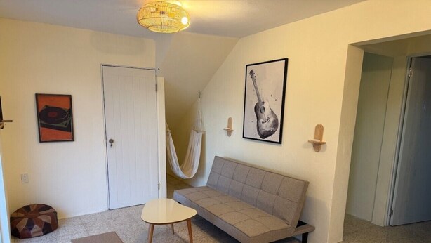 Quarto com sofá, mesa pequena, rede, porta e parede com pintura de guitarra.