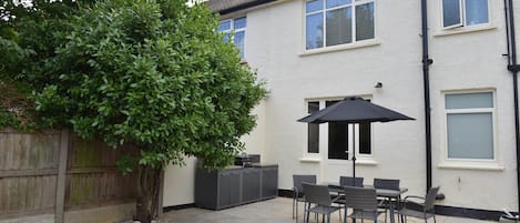 Un patio con una mesa, sillas, un paraguas negro y un árbol grande.