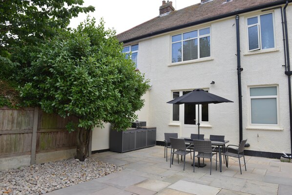 A patio with a table and chairs, a black umbrella, and a large tree.