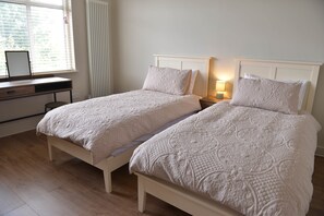 A bedroom with two single beds, a desk, and a window with blinds.