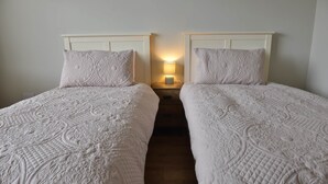 Habitación doble con dos camas, cada una con cabecera y mesita de noche con lámpara.