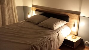 Una cama bien hecha con cabecera de madera, una mesita de noche con lámpara y un cuadro colgado en la pared.
