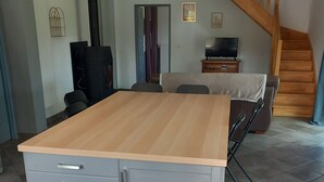 Una habitación con una mesa de madera, gabinetes grises, un sofá, un televisor y una escalera.