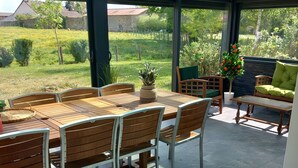 Un patio techado con mesa y sillas, una planta en maceta y vistas al follaje circundante.
