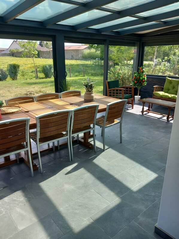 A covered patio with a table and chairs, a potted plant, and a view of the surrounding greenery. - 150-square-meter house with space for 3 bedrooms and sleeping arrangements for 8 people. Wooded, fenced-in lot; Veranda (Montigny-sur-Armançon)