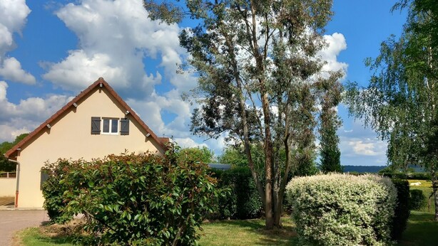 Una casa con techo inclinado, un pequeño porche y un césped cuidado con diversos arbustos y un árbol grande.