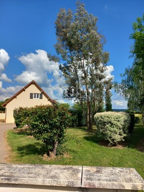 Ein Haus mit geneigtem Dach, einer kleinen Veranda und einem gepflegten Rasen mit verschiedenen Sträuchern und einem großen Baum.