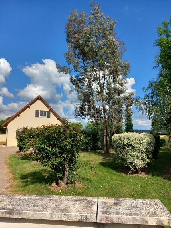 A house with a sloped roof, a small porch, and a well-maintained lawn with a variety of shrubs and a large tree.