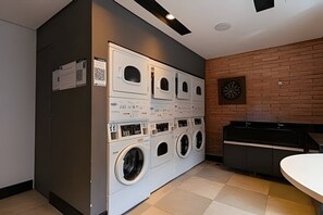 Ein Waschraum mit mehreren Waschmaschinen und Trocknern, einem Waschbecken und einer Dartscheibe an der Wand.