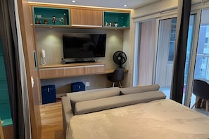 Ein modernes Schlafzimmer mit Bett, Fernseher, Ventilator und integrierten Stauraum.