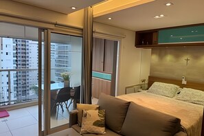 Ein Schlafzimmer mit einem Bett, einem Sessel und Blick auf eine Stadtlandschaft durch eine Schiebetür.