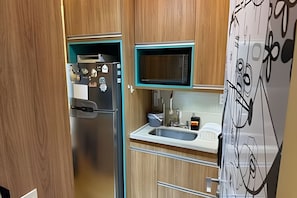 Eine kompakte Küche mit integriertem Mikrowellenherd, einem Edelstahlkühlschrank und einer Spüle.