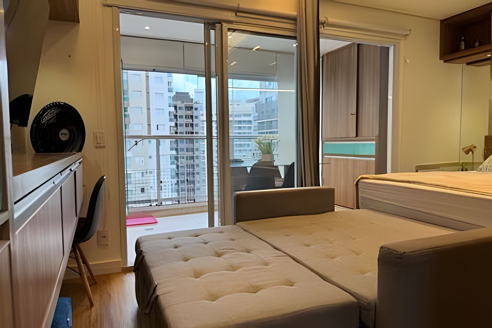 Una camera da letto con un letto grande, una scrivania e una sedia. C'è una porta scorrevole in vetro che dà su un balcone con vista sugli edifici.